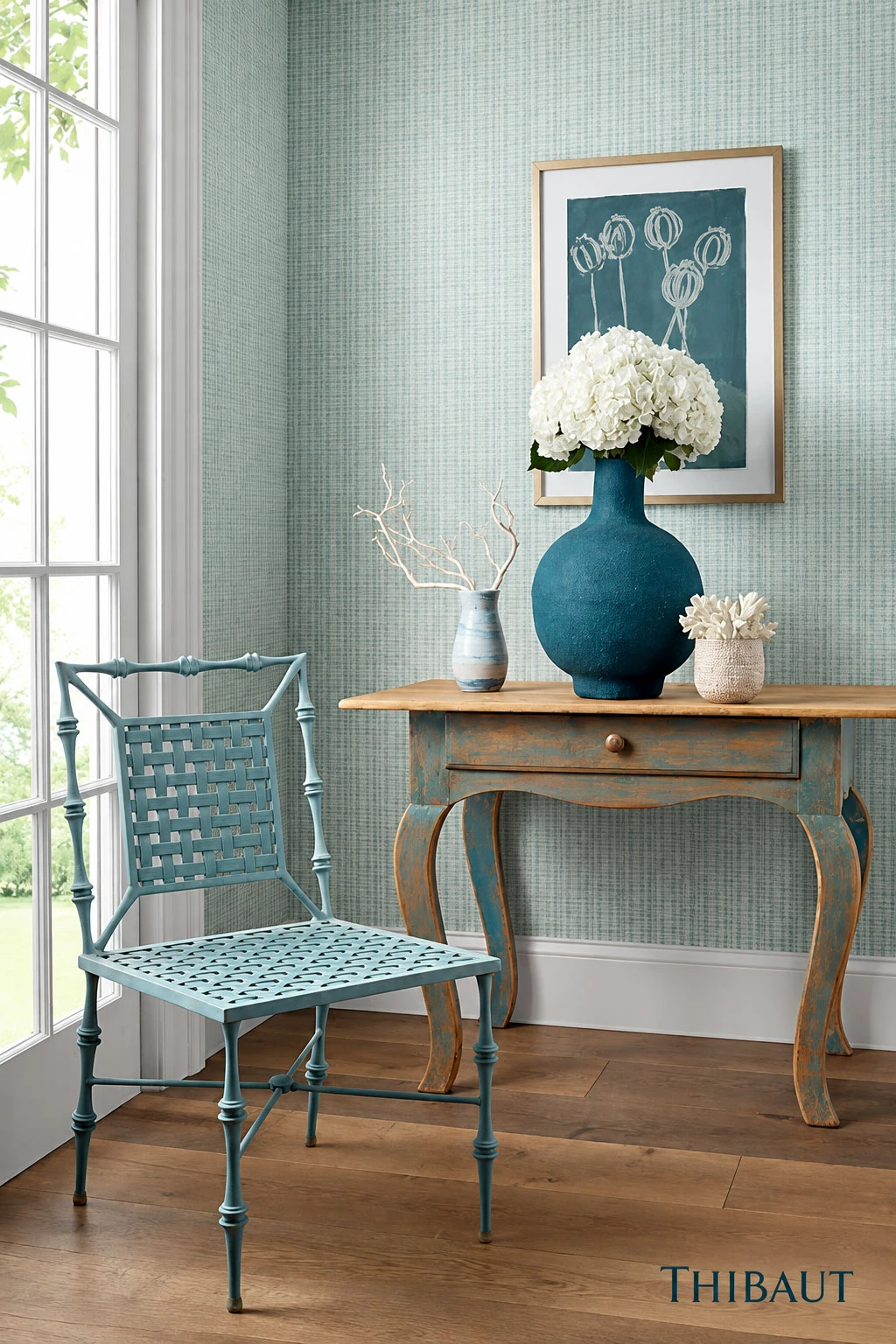 Pale aqua textured wallcovering behind blue furnishings, floral artwork, and a sunlit window